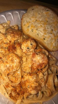 a plate with pasta, meat and cheese on it next to a piece of bread