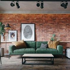 a living room with brick walls and green couches in it, along with pictures on the wall