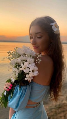 a woman with flowers in her hair is standing on the beach near the water at sunset