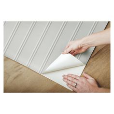 two hands are opening up a piece of paper on a wooden table with a white wall in the background