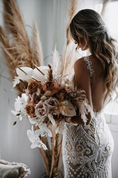 a woman in a wedding dress holding a large bouquet with flowers and feathers on it