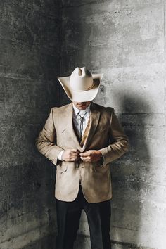 a man in a suit and cowboy hat standing next to a wall with his hands on his pockets