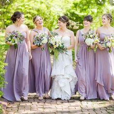 a group of women standing next to each other in front of trees and bushes with bouquets