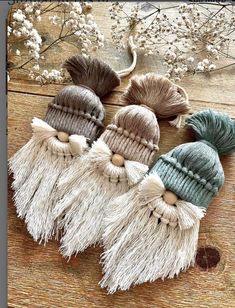 three knitted hats with tassels are sitting on a wooden table next to flowers