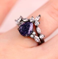 a woman's hand holding a ring with a purple stone surrounded by white diamonds