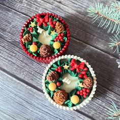 two decorated cupcakes sitting on top of a wooden table next to a pine tree