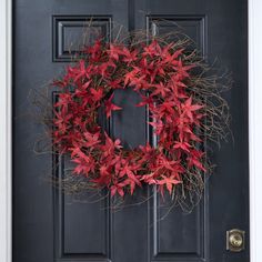 a wreath is hanging on the front door with red leaves and branches around it,