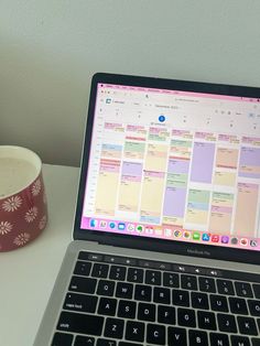 an open laptop computer sitting on top of a white desk next to a cup of coffee