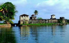 an old castle sitting on top of a lush green field next to the ocean with palm trees