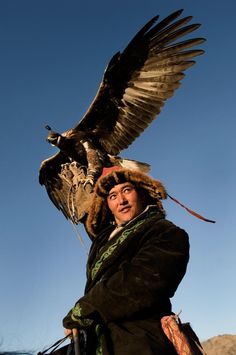 a man holding an eagle on his arm with the sky in the backgroud