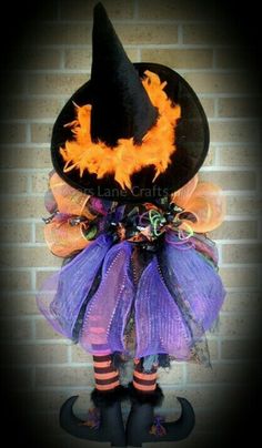 a witch costume with purple and orange tulle, black hat and striped socks is hanging on a brick wall