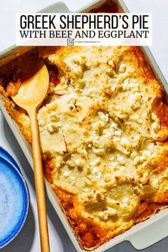 a casserole dish with cheese and eggplant in it next to a wooden spoon