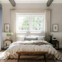 a bed sitting under a window next to a wooden foot stool in front of a window