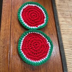 two crocheted watermelon coasters sitting on top of a wooden table