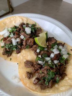 two tacos with meat, onions and cilantro on a white plate