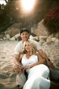 a man sitting next to a woman on top of a sandy beach