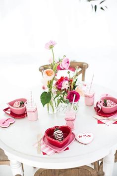 a white table topped with pink plates and cups filled with flowers on top of it