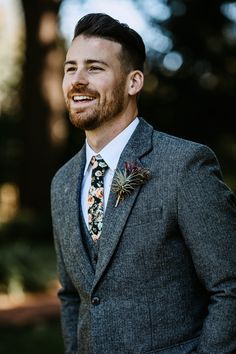 a man in a suit and tie smiles at the camera while wearing a flower boutonniere