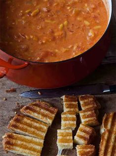 grilled french toast and tomato soup in a red pot on a wooden table next to a cutting board