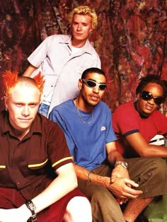 four young men sitting next to each other in front of a colorful wall wearing sunglasses