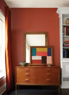 a dresser with a mirror on top of it next to a bookshelf and window