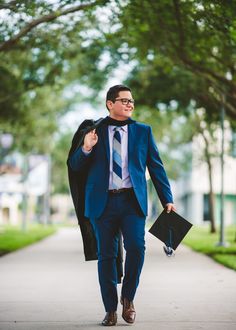 a man in a blue suit and tie walking down a sidewalk with a briefcase on his shoulder