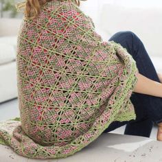 a woman is sitting on the floor wrapped in a crochet shawl and looking at the camera