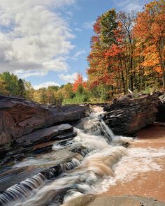 a river running through a forest filled with lots of trees covered in fall foliage and rocks