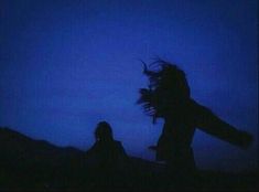 two people are silhouetted against the night sky with their arms in the air and one person is throwing a frisbee