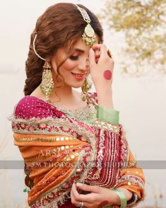 a woman in an orange and red dress is holding her hand up to her ear