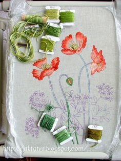 some spools of thread sitting on top of a piece of cloth with flowers painted on it