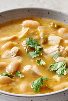 a white bowl filled with soup and garnished with cilantro, parsley