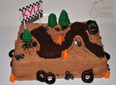 a cake that is made to look like a dirt track with trees and flags on top