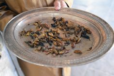 a person holding a metal plate with food on it and some other things in the tray