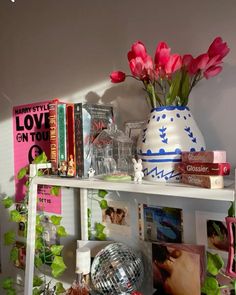 a white shelf topped with lots of books and vases filled with pink tulips