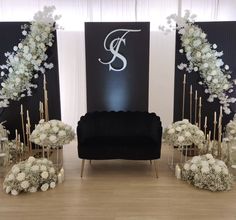 an arrangement of white flowers and branches in front of a black chair with the letter s on it