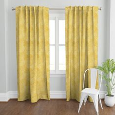 a white chair sitting in front of a window with yellow curtains on top of it