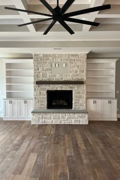 an empty living room with white built in bookshelves and a large stone fireplace