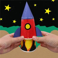 two hands holding a paper rocket ship in front of a black background with stars on it