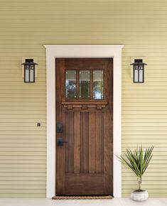 a wooden door on the side of a yellow house with two light fixtures above it