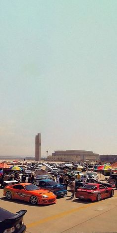 a parking lot filled with lots of different colored cars next to a tall building in the distance