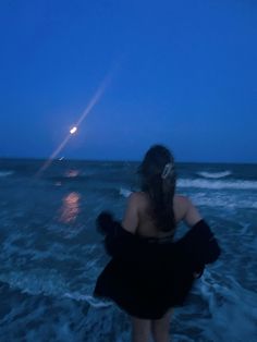 a woman standing in the ocean at night with her back to the camera, looking into the distance