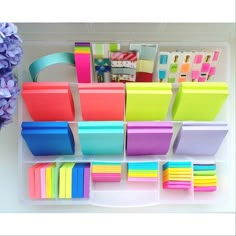 several different colored sticky notes are arranged on a white tray with purple flowers in the background