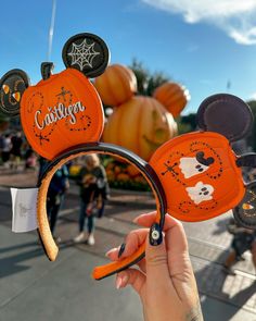 someone is holding up mickey mouse ears at the disneyland halloween parade, with pumpkins in the background