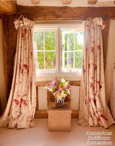 a vase with flowers sitting on top of a table in front of a curtained window