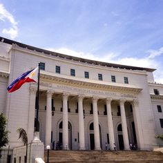 a large white building with columns and a flag flying in front of it on a sunny day