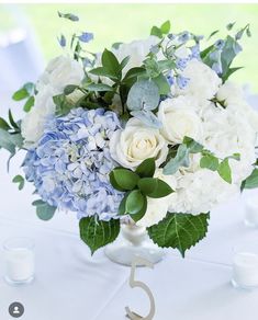 a vase filled with white and blue flowers sitting on top of a table next to candles