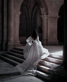 a woman in a long white dress is sitting on some steps and looking off into the distance