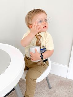 a little boy sitting at a table with a coffee cup in front of his face