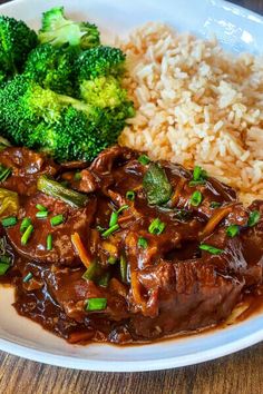 a white plate topped with beef and broccoli next to rice on a wooden table